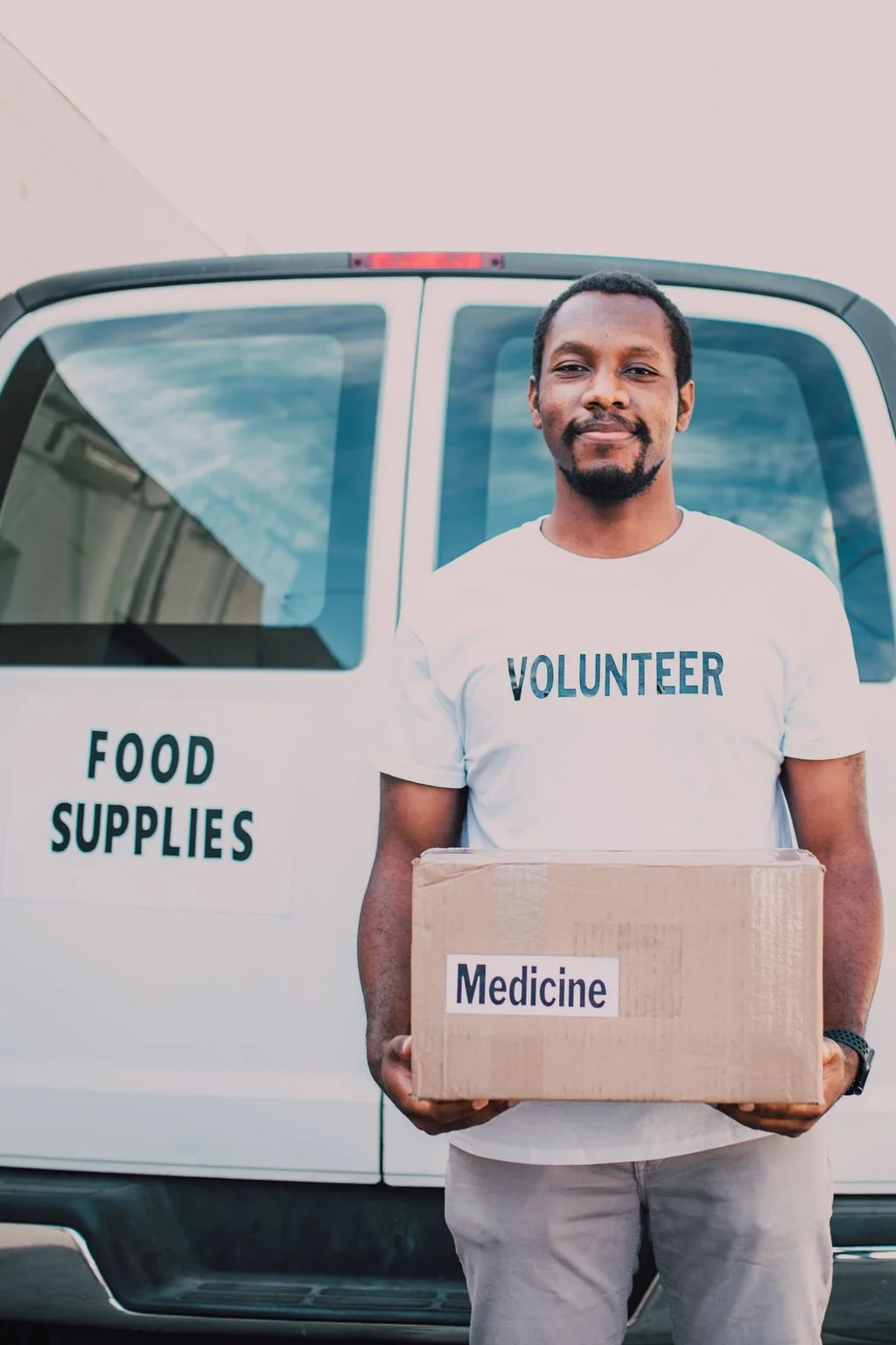 Volunteer in front of a food-supplies van carrying a Medicine relief box — community storm relief