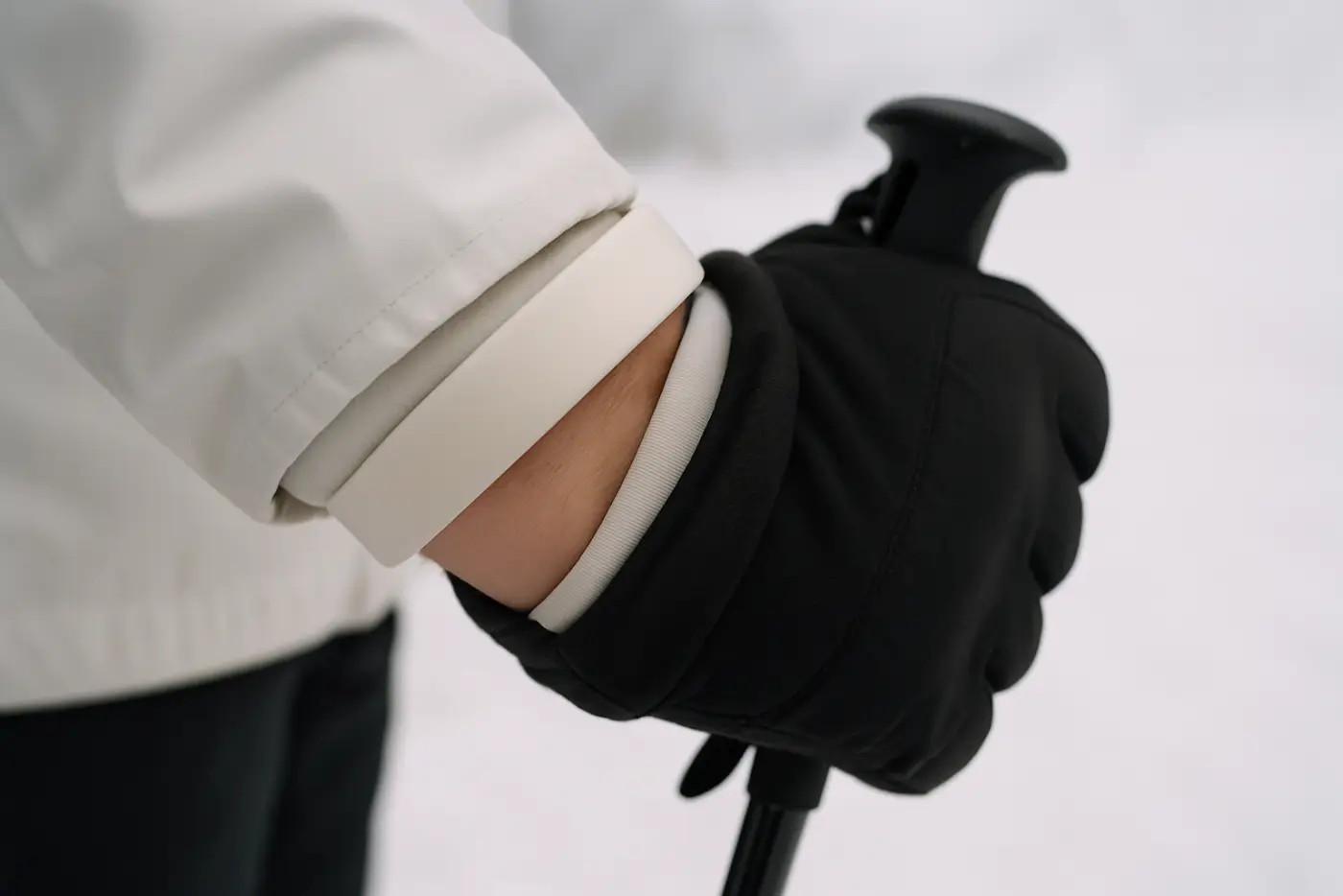 A plain wide silicone wristband worn over the cuff of a plain ski jacket, gloved hand gripping a ski pole