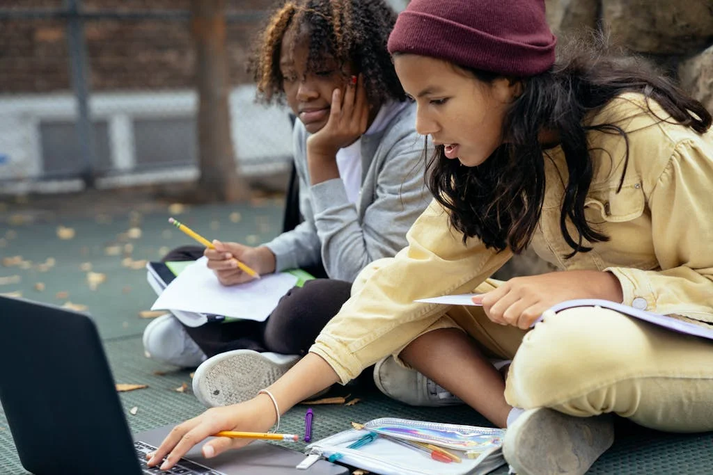 Two diverse students collaborating in a school inclusion activity with notebooks and laptop