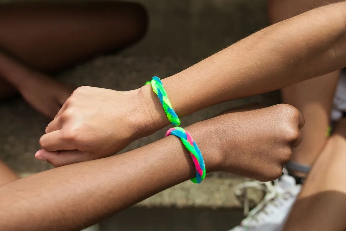 Two wrists wearing bright multicolour swirl silicone wristbands in green, blue, pink and yellow