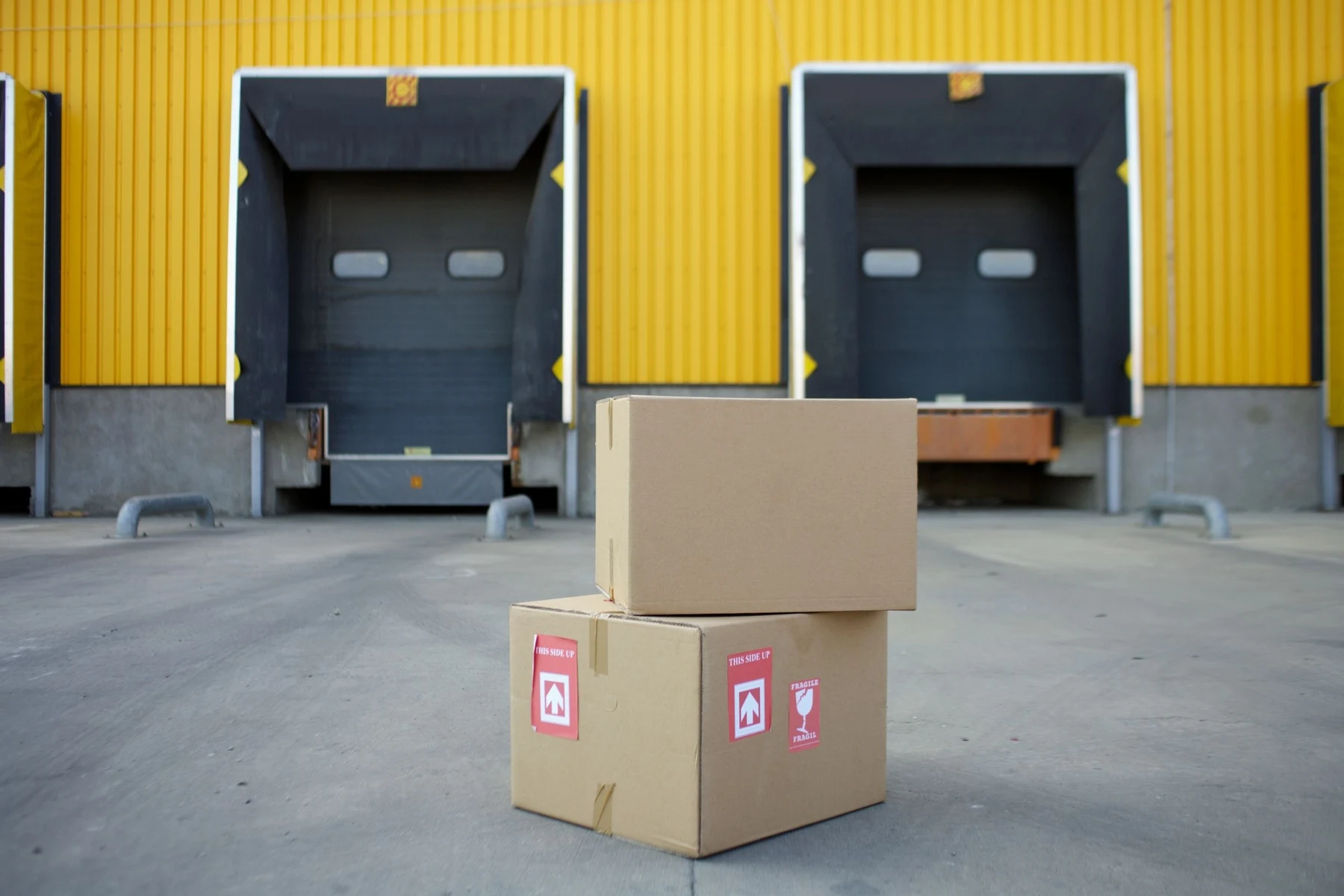 Two cardboard cartons on the ground in front of yellow warehouse loading dock doors
