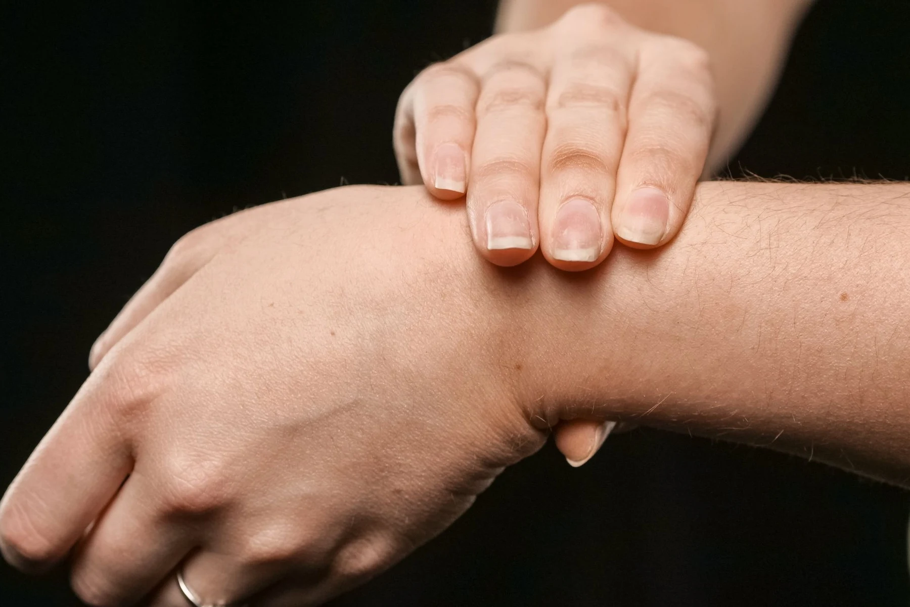 Close-up of one hand resting against the bare skin of the opposite wrist on a dark background