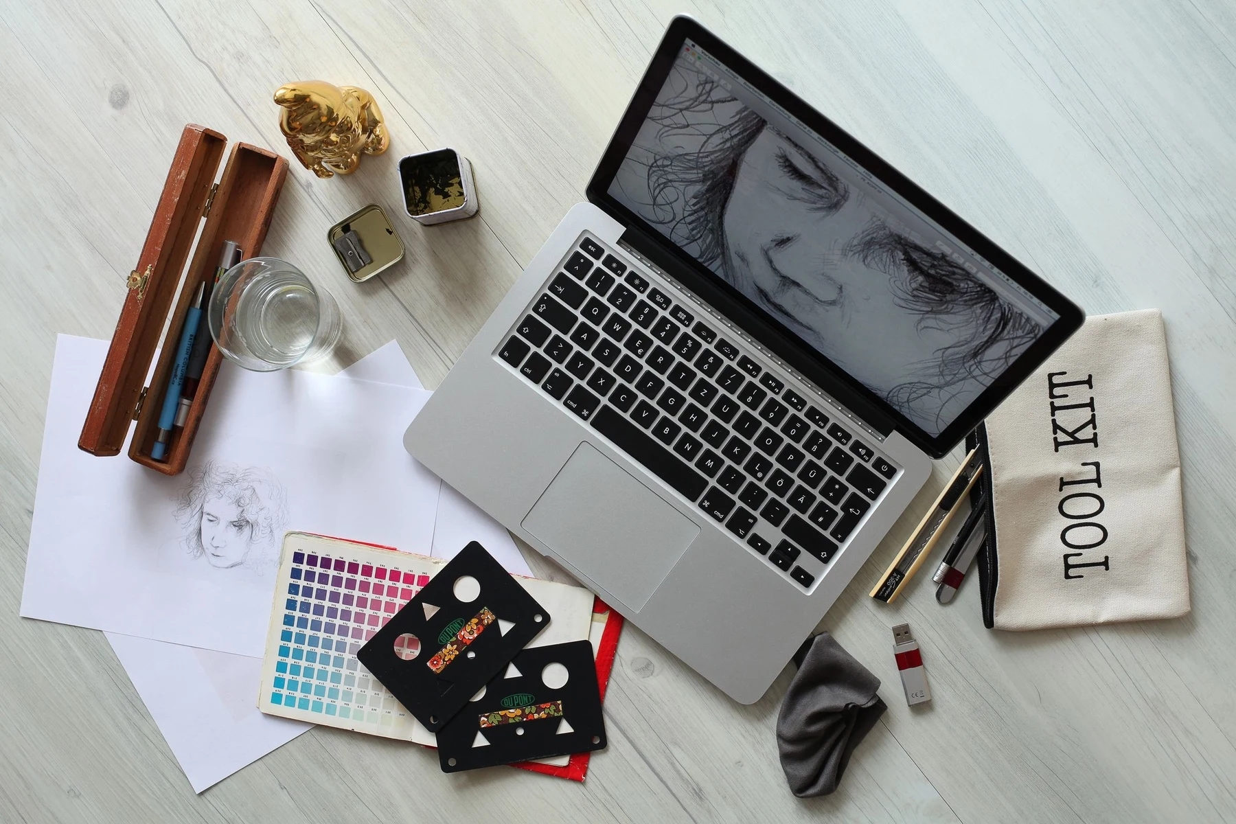 A designer desk from above with a laptop showing artwork, colour swatch cards, pens and a sketch pad
