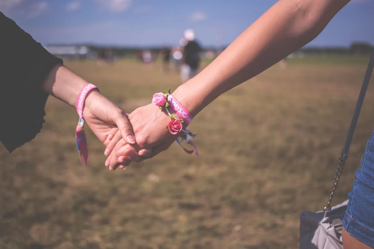 Two people holding hands outdoors, both wearing worn pink fabric festival wristbands