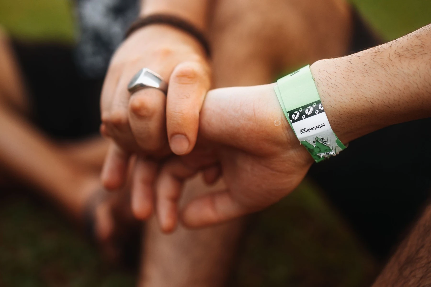 Close-up of two clasped wrists outdoors, one wearing a green printed event entry wristband