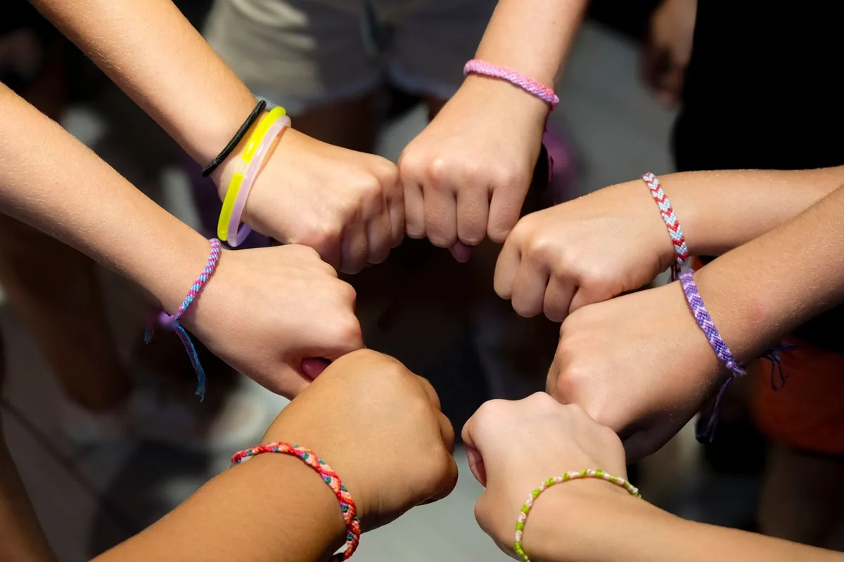 A circle of wrists belonging to several people, each wearing wristbands of different widths and colours