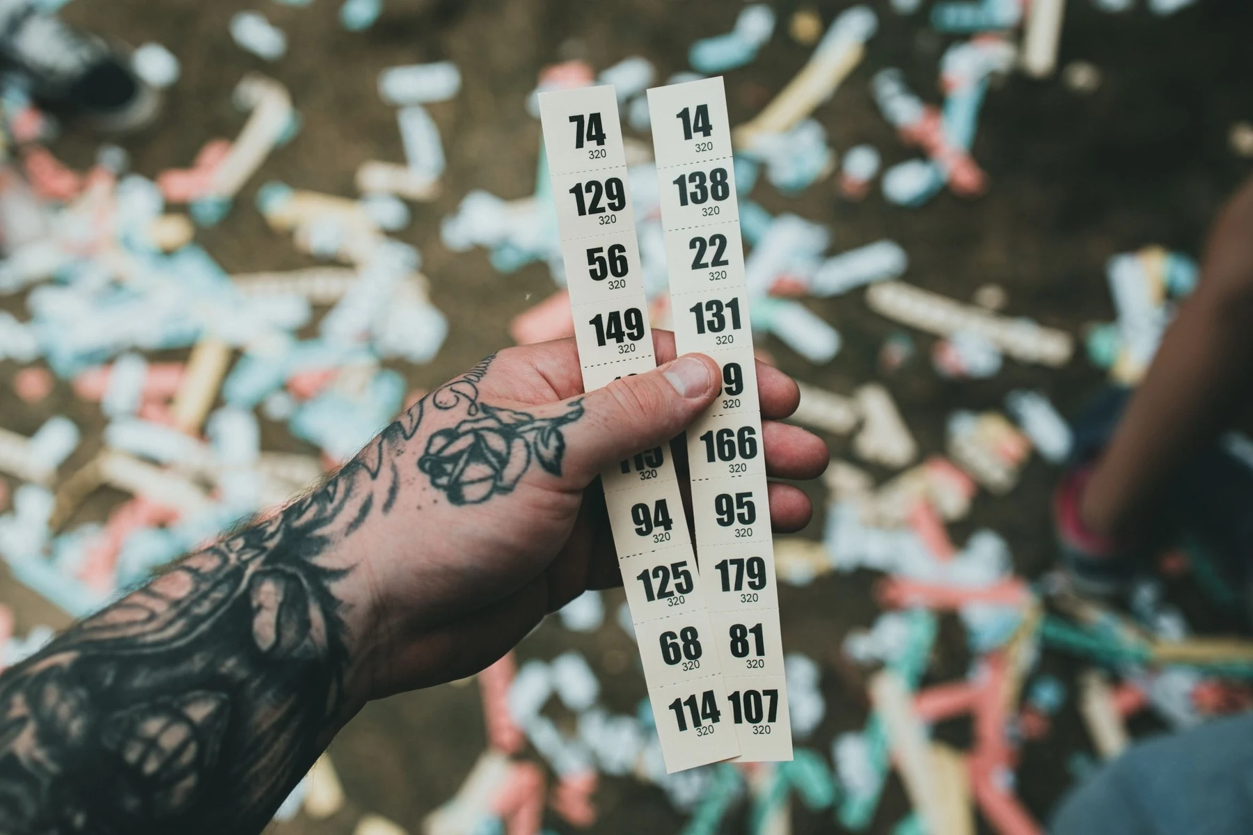 A hand holding a strip of numbered paper entry tickets above scattered ticket stubs on the ground