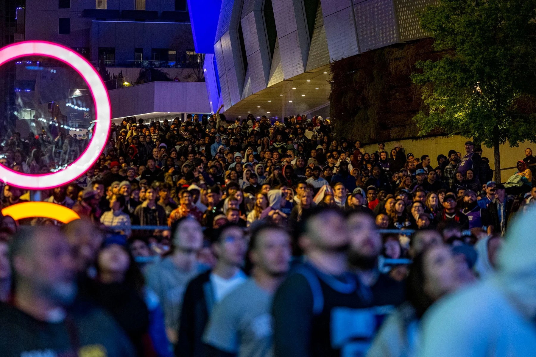 A large crowd at an outdoor night event lit by neon and coloured lighting