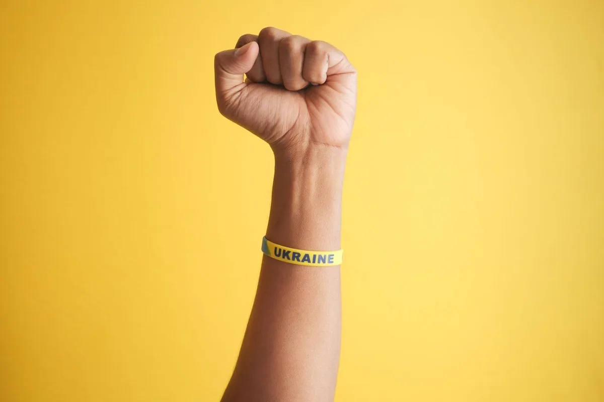 A raised fist wearing a yellow silicone wristband with printed lettering against a plain background