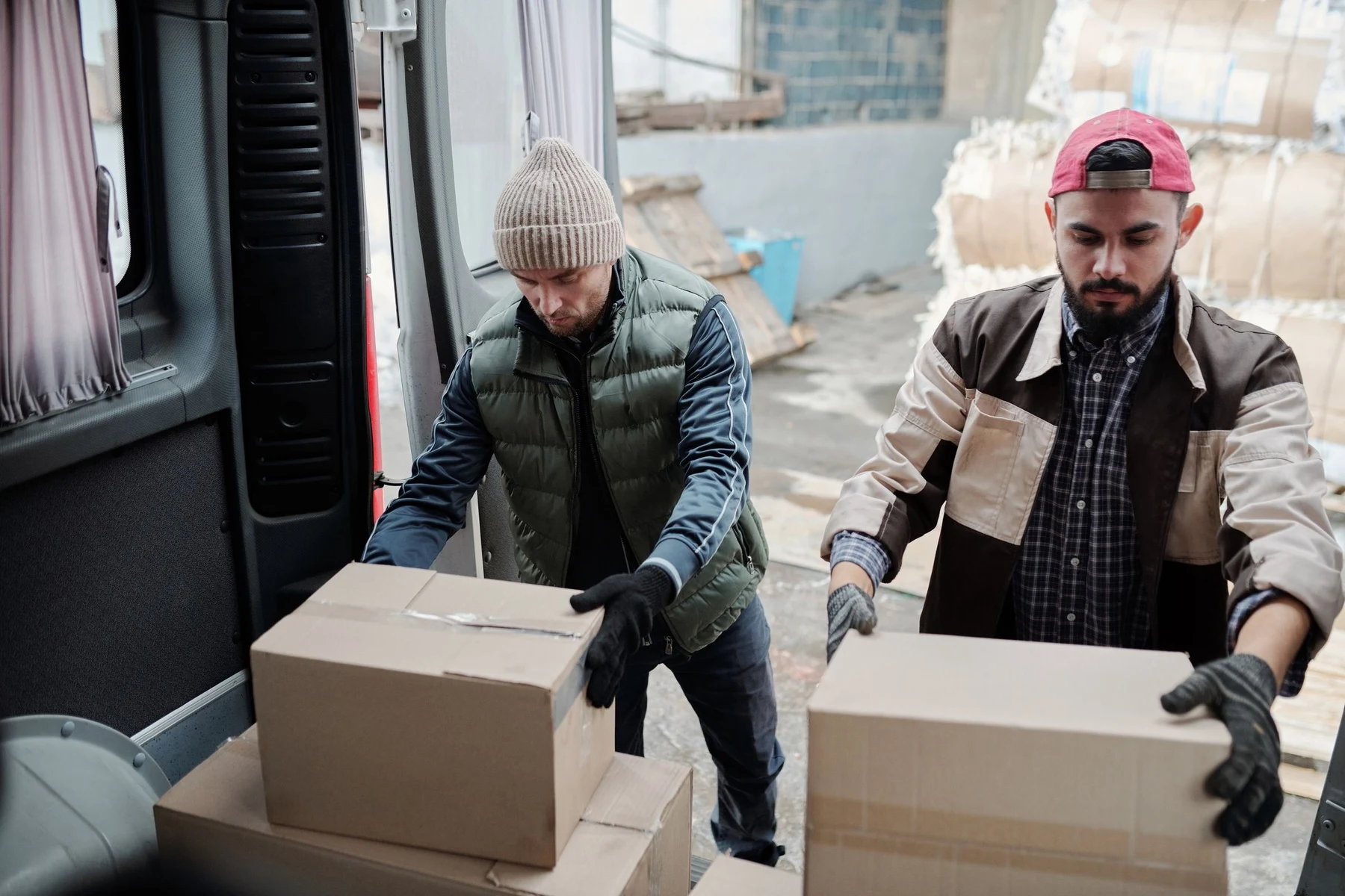 Two workers loading cardboard packages into the back of a delivery van