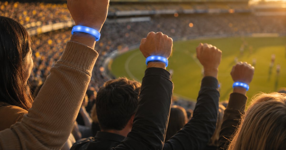 Crowd of 50,000 raising LumoSynch LED wristbands at stadium scale during a broadcast moment
